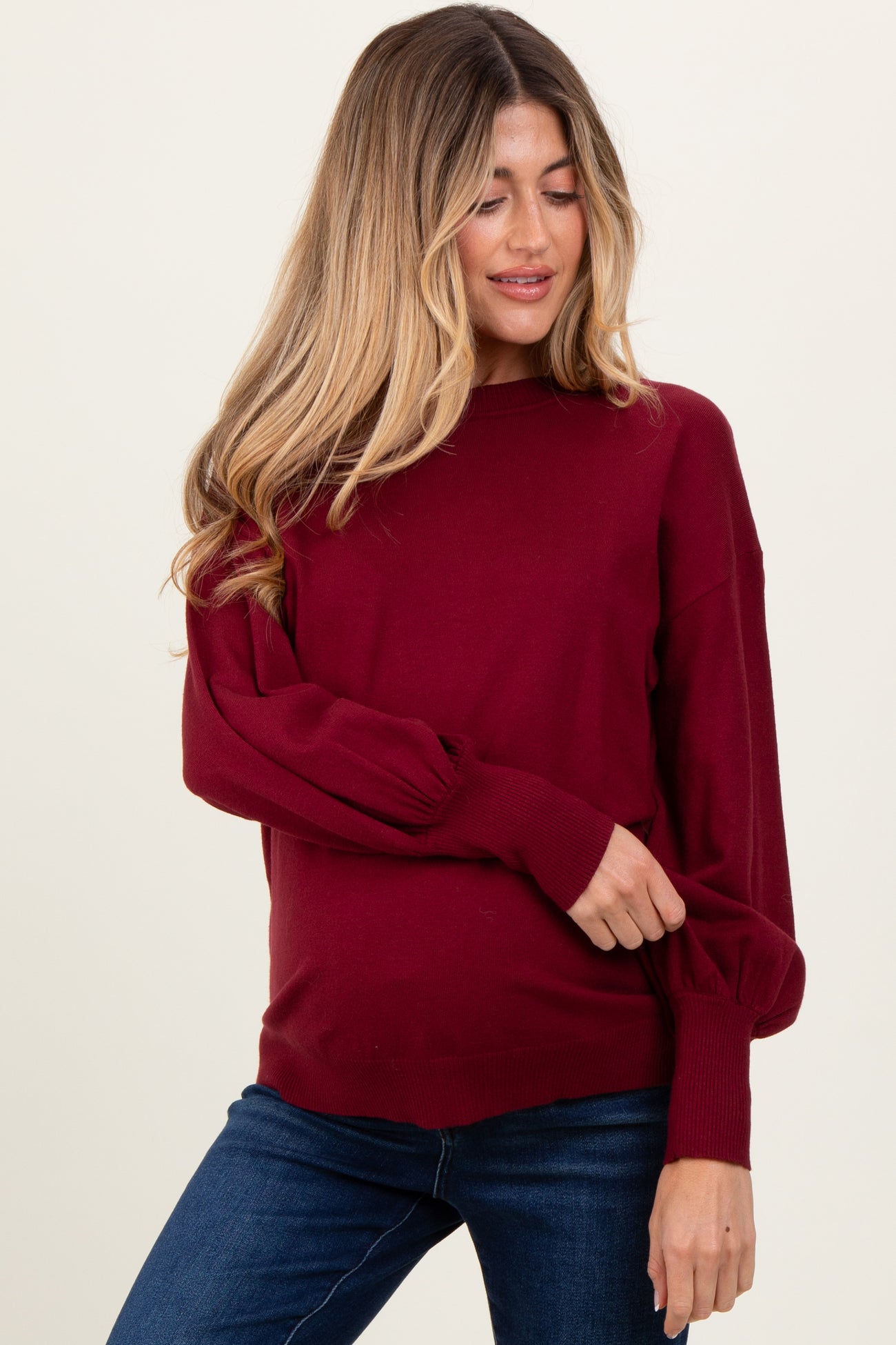 woman wearing a burgundy maternity sweater with balloon sleeves and holding her baby bump