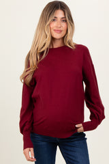 woman wearing a burgundy maternity sweater with ribbed sleeves and a visible baby bump