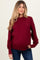 woman wearing a burgundy maternity sweater with ribbed sleeves and a visible baby bump