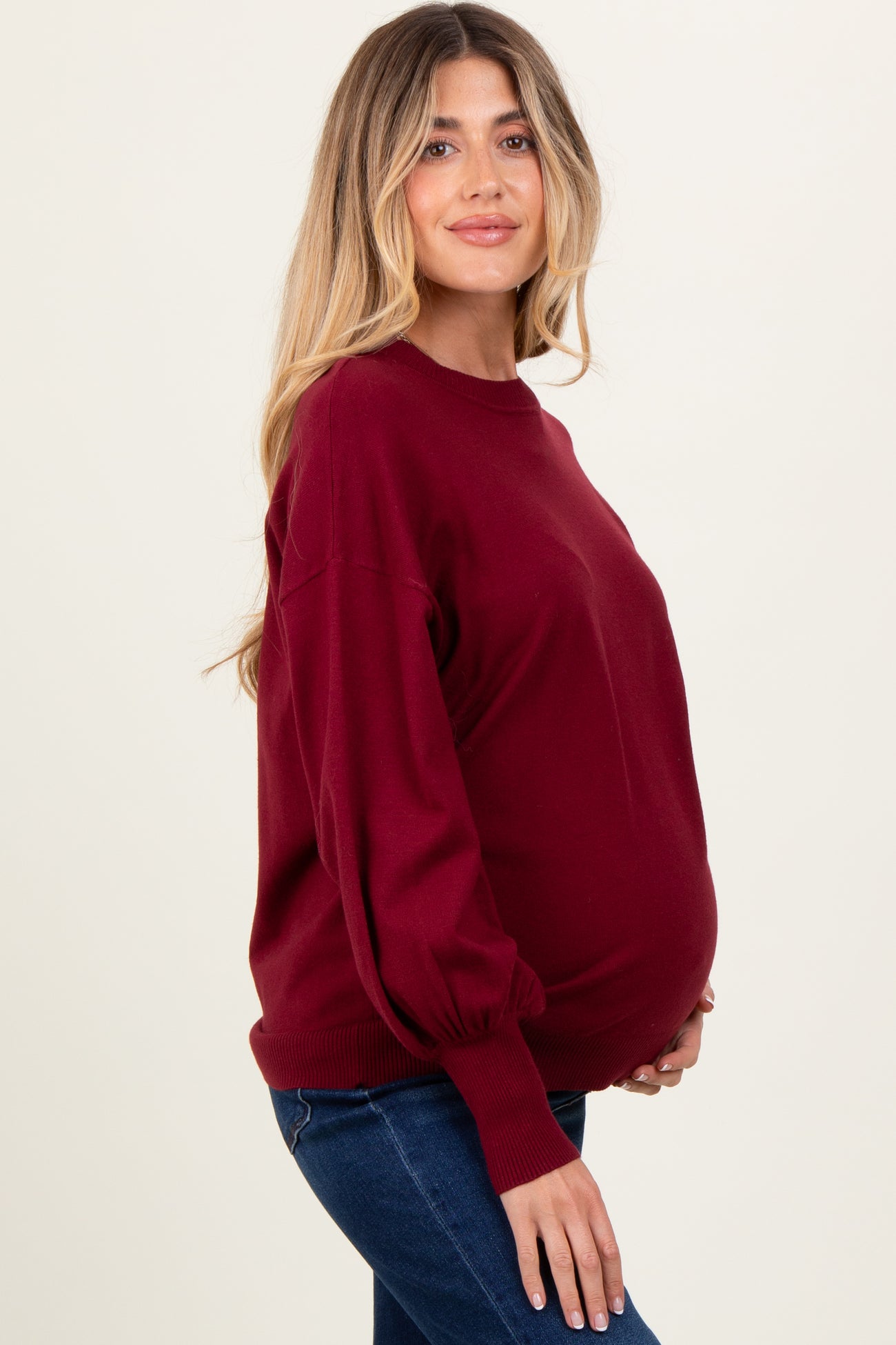 woman wearing a burgundy maternity sweater with balloon sleeves and showing her baby bump