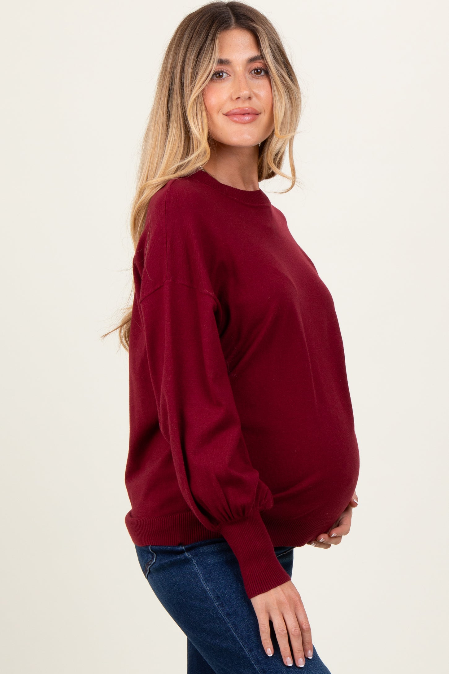 woman wearing a burgundy maternity sweater with balloon sleeves and showing her baby bump
