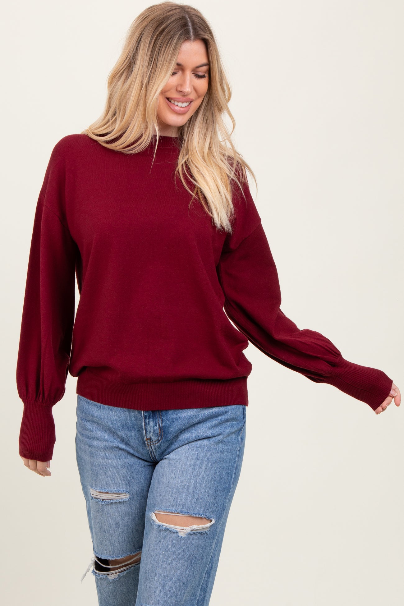 woman wearing a burgundy pullover sweater with balloon sleeves and paired with distressed light blue jeans