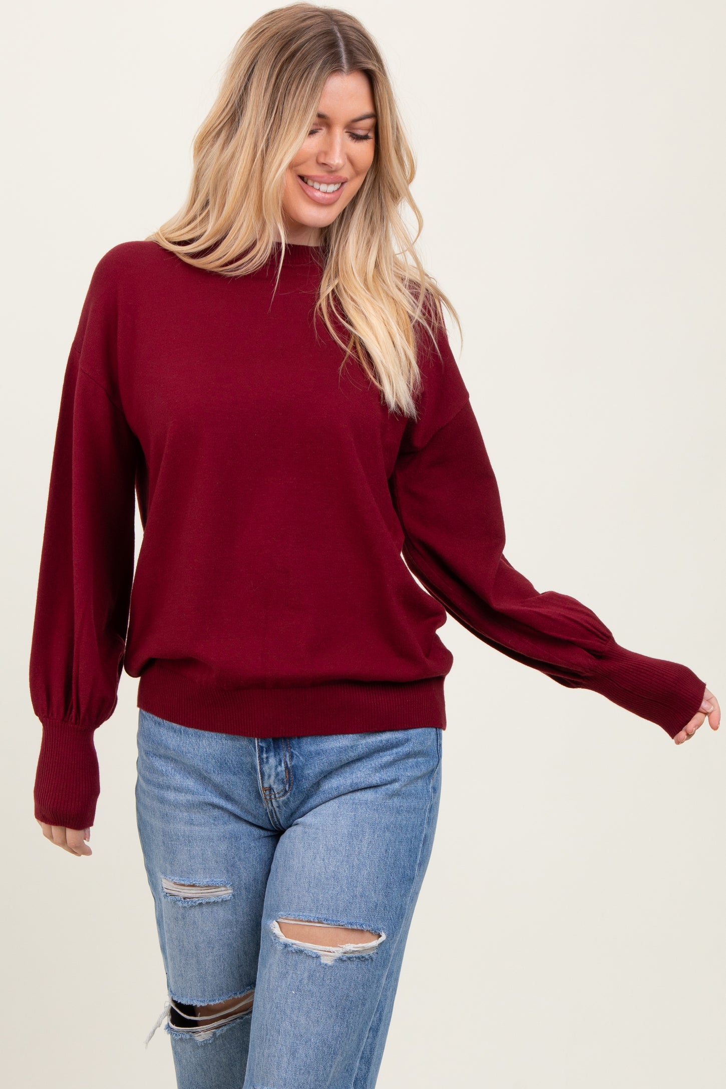 woman wearing a burgundy pullover sweater with balloon sleeves and paired with distressed light blue jeans
