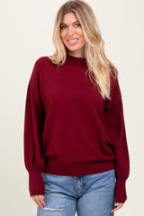 woman wearing a burgundy oversized sweater with balloon sleeves and paired with light blue distressed jeans