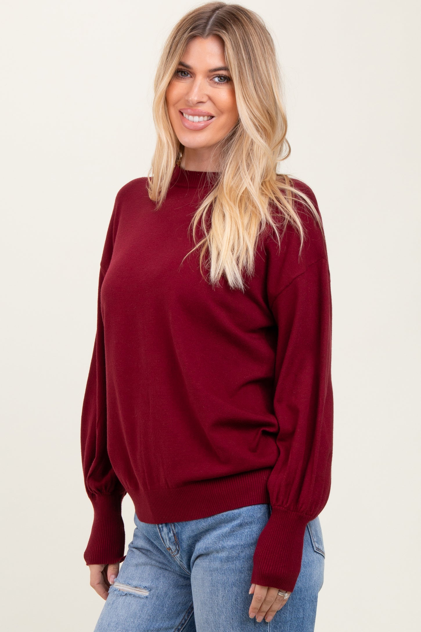 woman wearing a burgundy oversized sweater with balloon sleeves and a relaxed fit, paired with light blue jeans