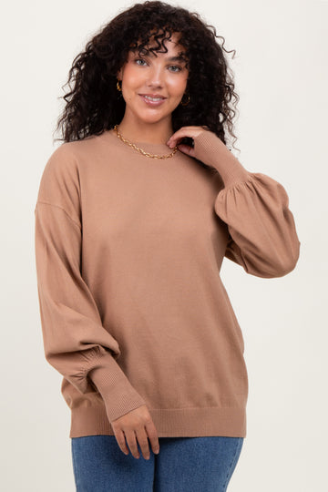 woman wearing a tan oversized sweater with puff sleeves and a relaxed fit, posing with a smile