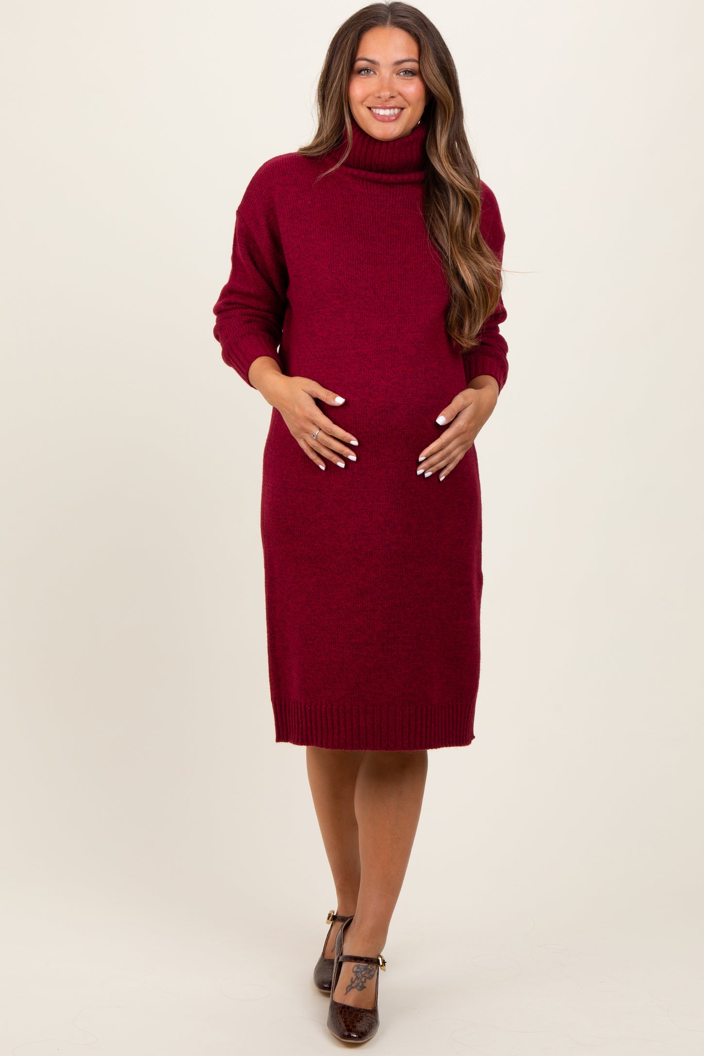 woman wearing a burgundy turtleneck maternity sweater dress and cradling her baby bump