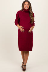 woman wearing a burgundy turtleneck maternity sweater dress and cradling her baby bump