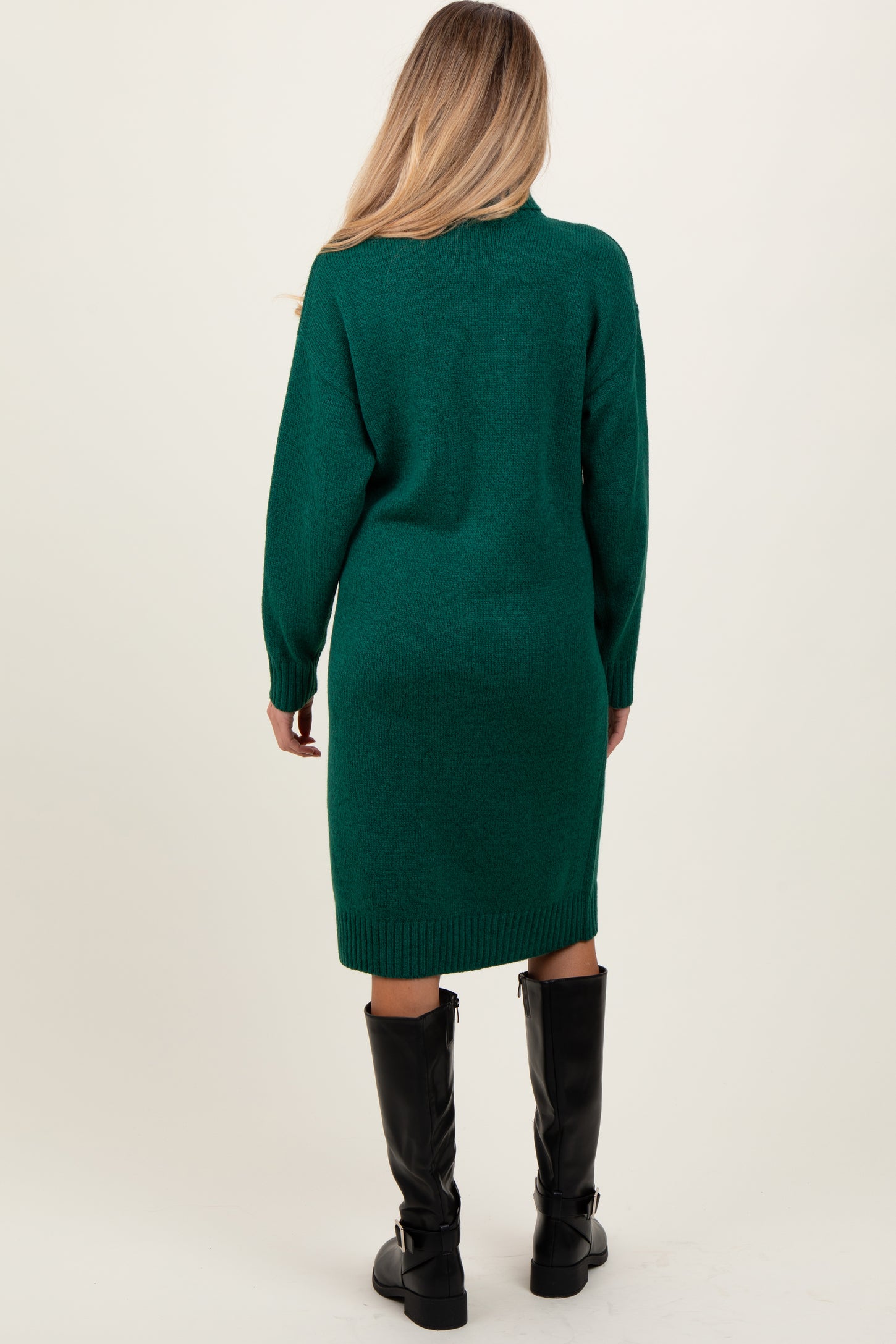 woman wearing a dark green long sleeve sweater dress, featuring a relaxed fit and knee-length, with black knee-high boots