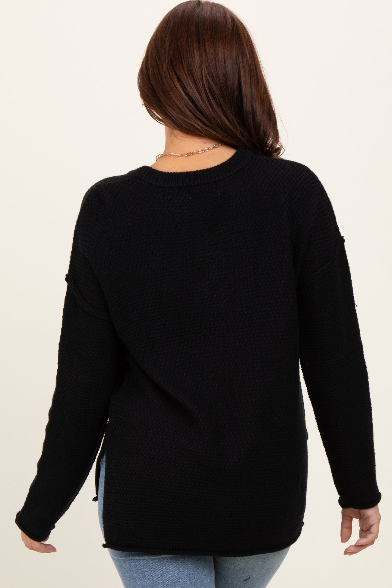 woman wearing a black waffle knit sweater with side slits, view from the back
