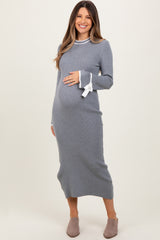 woman wearing a gray ribbed maternity dress with a bow detail at the sleeves and holding her baby bump