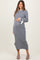 woman wearing a gray ribbed maternity dress with a bow detail at the sleeves and holding her baby bump