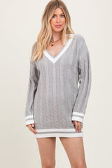 woman wearing a gray cable-knit mini sweater dress with white trim and a deep v-neckline
