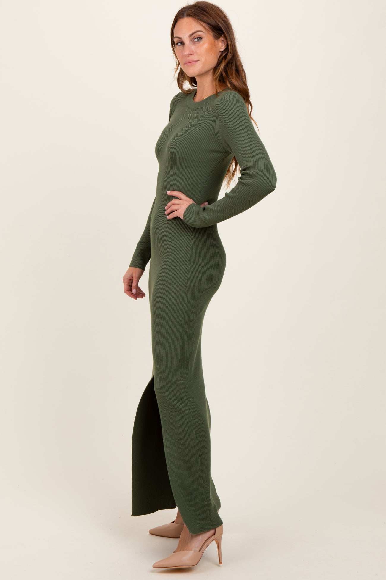 woman wearing a dark green ribbed maxi dress with long sleeves and a side slit, paired with nude heels