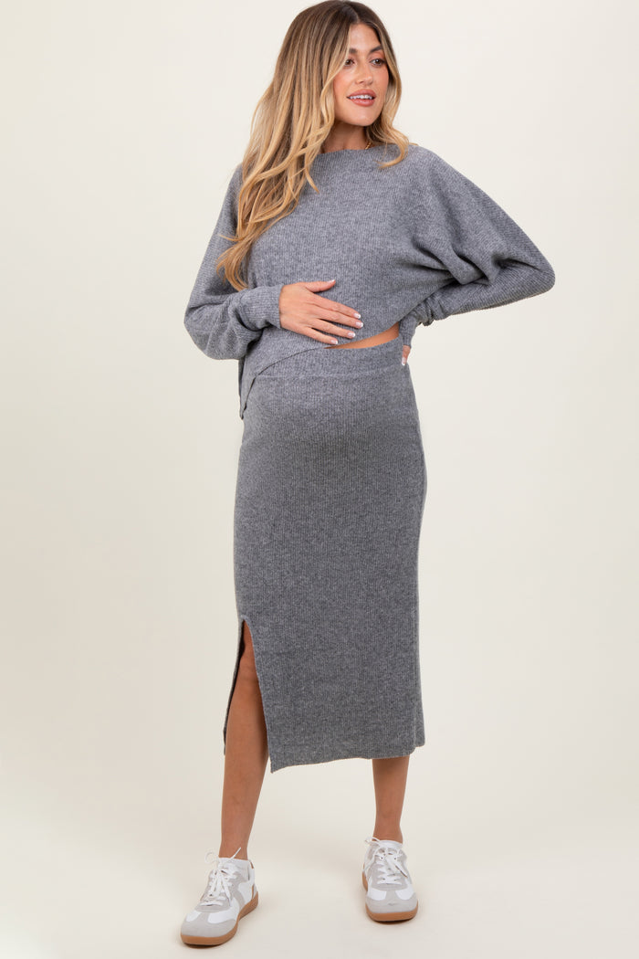 woman wearing a gray maternity sweater and matching midi skirt, gently holding her baby bump