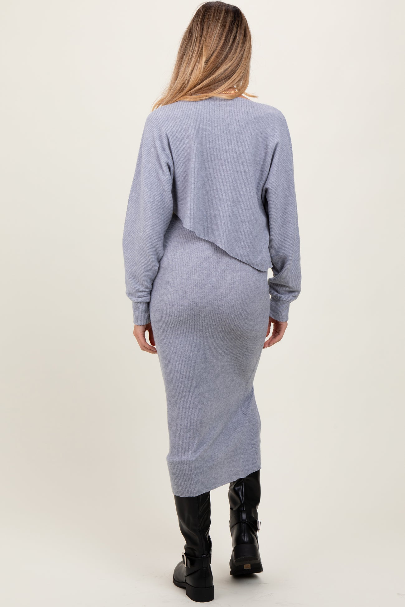 woman wearing a light gray long sleeve maternity dress with a draped back, fitted silhouette, and knee-high black boots