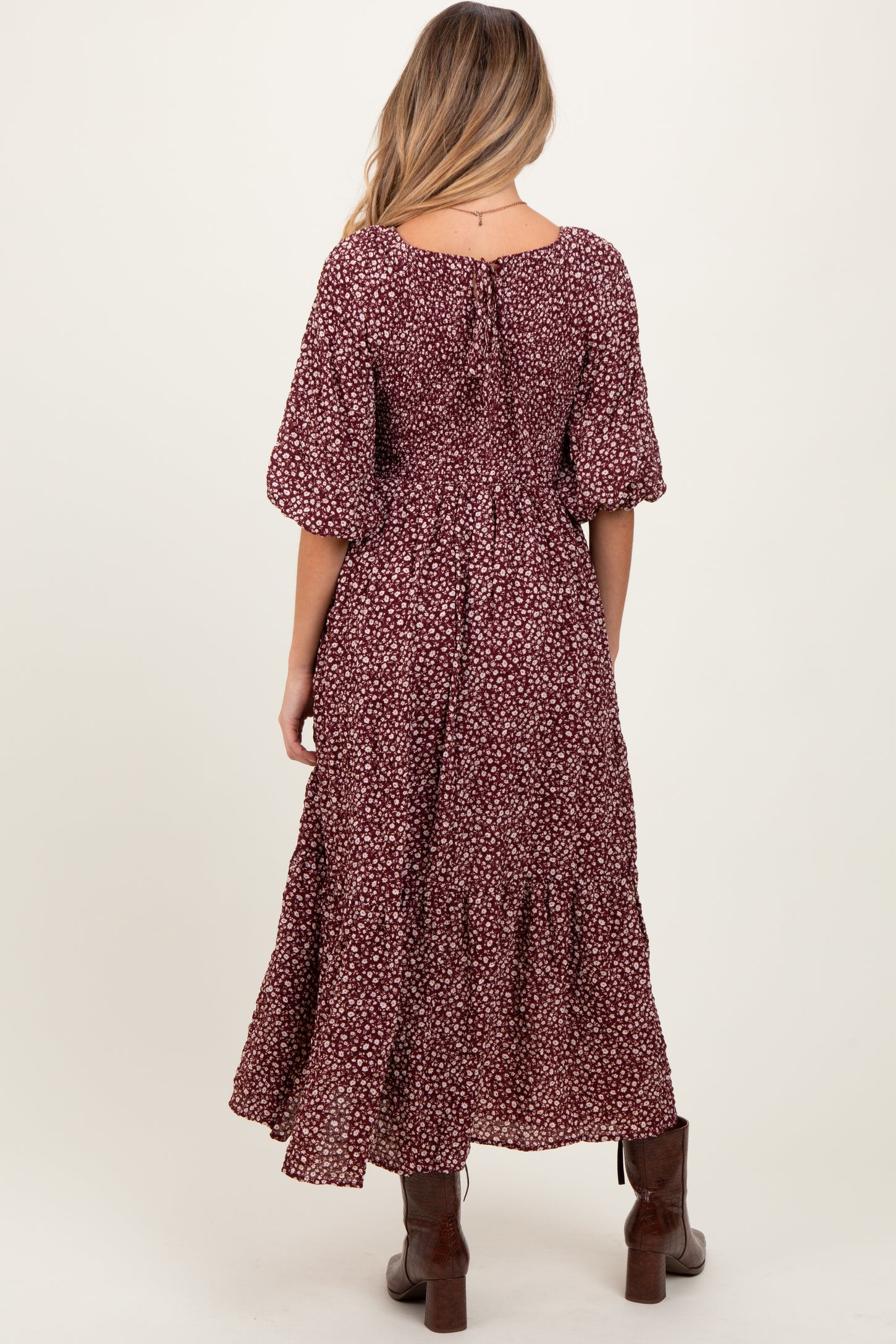woman wearing a burgundy floral maternity maxi dress with short puff sleeves and a tiered skirt, showing the back view