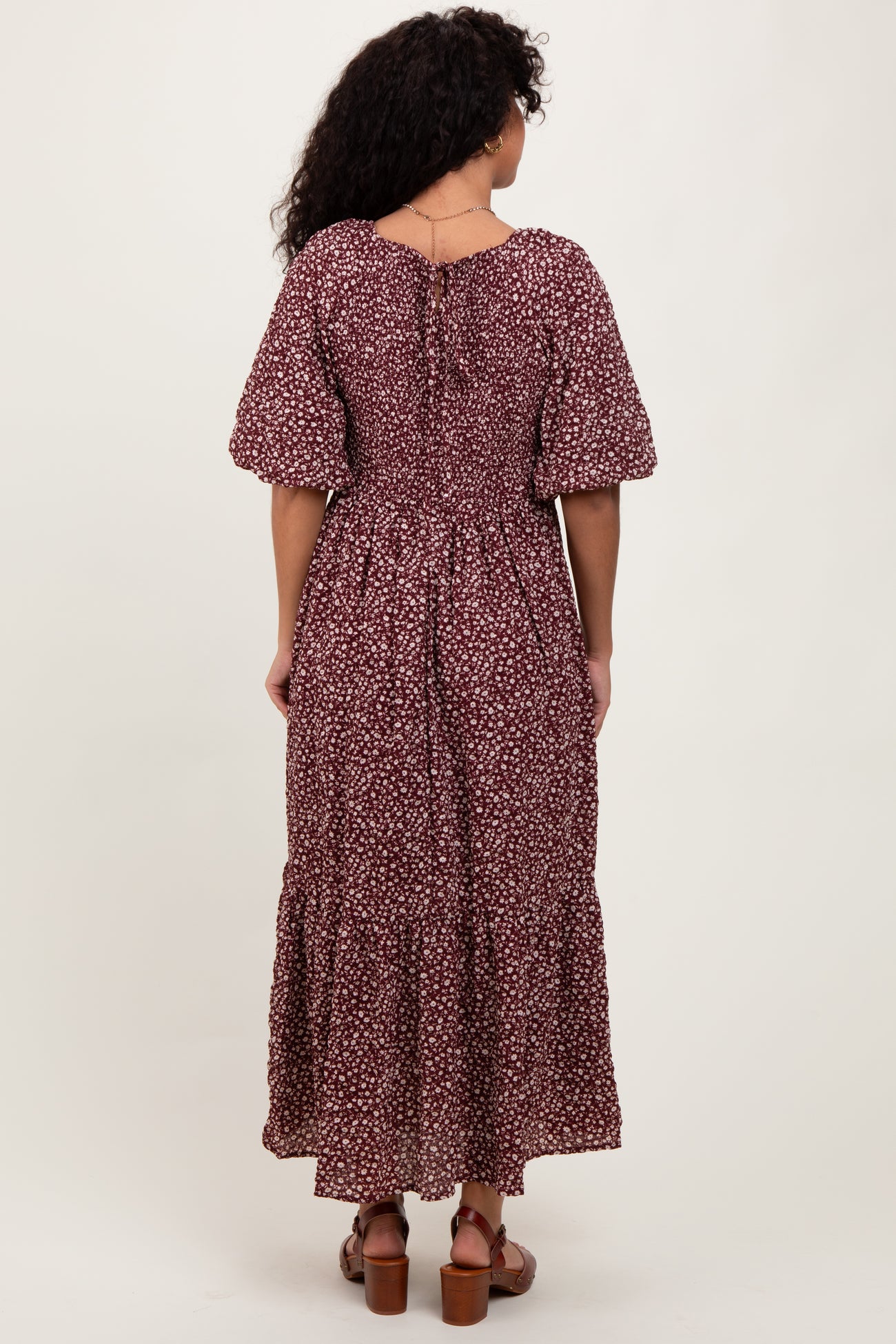 woman wearing a burgundy floral maxi dress with short puff sleeves and a tiered skirt, viewed from the back