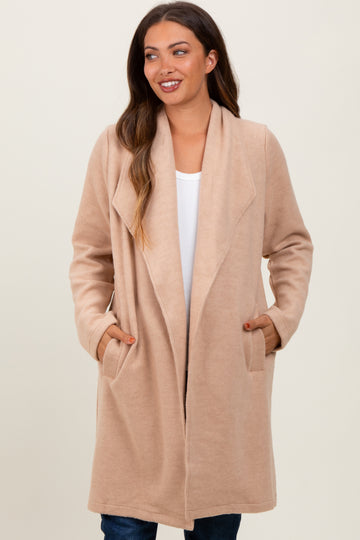 woman wearing a beige maternity wrap coat with pockets, styled open over a white top and denim jeans