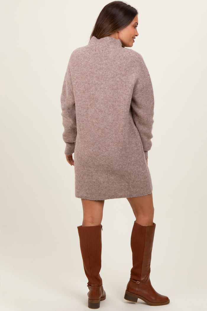 woman wearing a taupe knit maternity sweater dress with a high collar and long sleeves, paired with brown knee-high boots