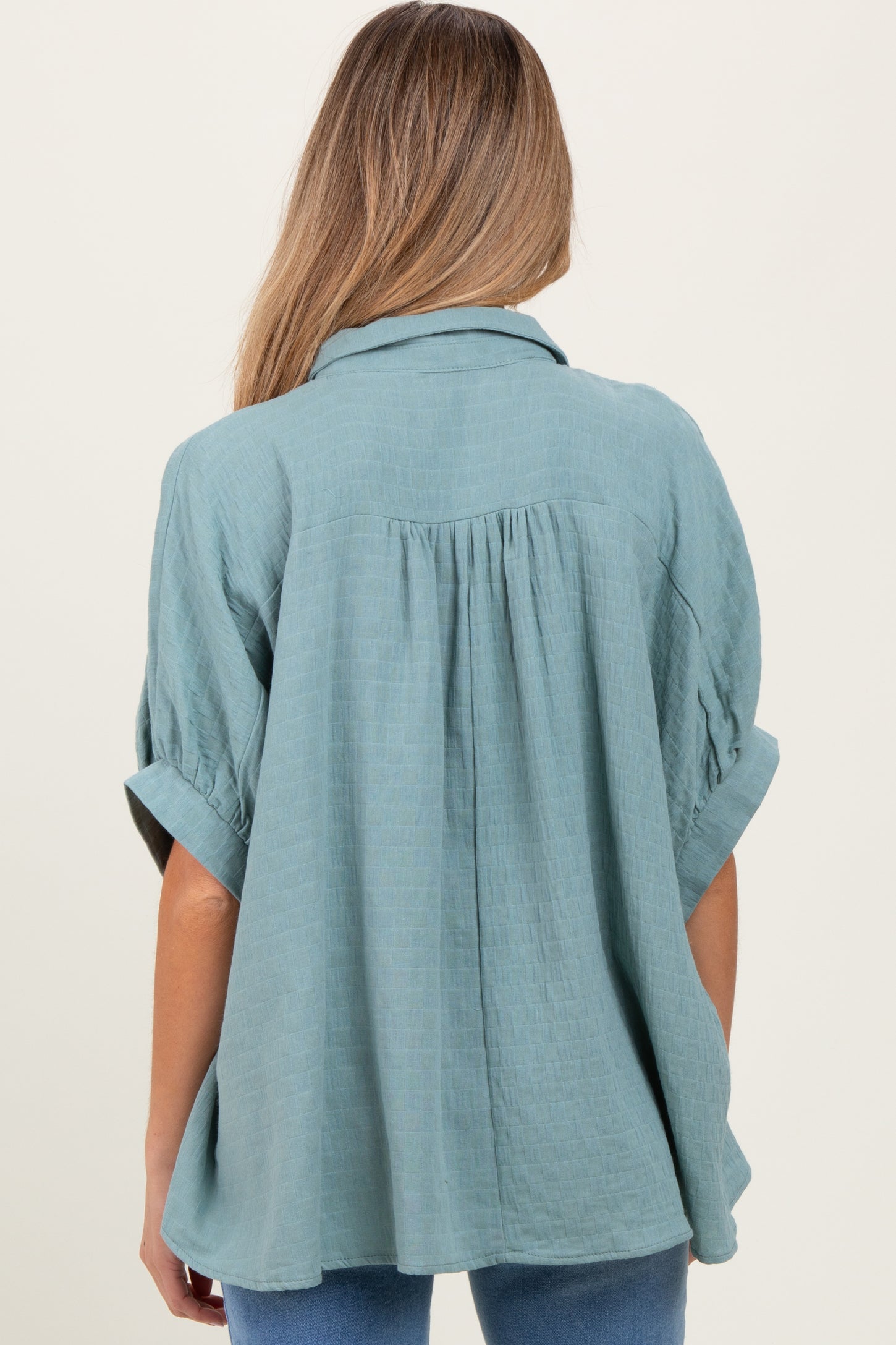woman wearing a loose-fitting teal maternity top with rolled sleeves and a pleated back