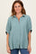 woman wearing a relaxed fit light green button-up shirt with rolled sleeves and a textured finish