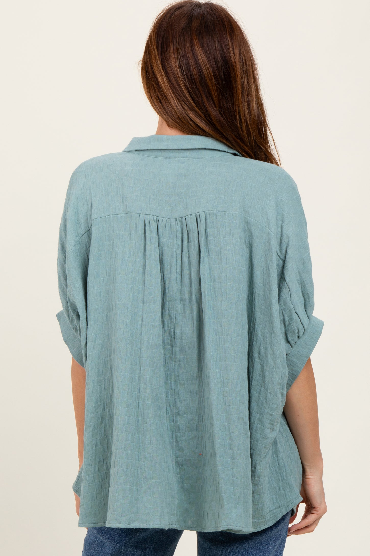 woman wearing a loose-fitting light blue shirt with a back pleat and rolled sleeves