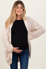 woman wearing a cream oversized knitted maternity cardigan and holding her baby bump, paired with a black top and jeans