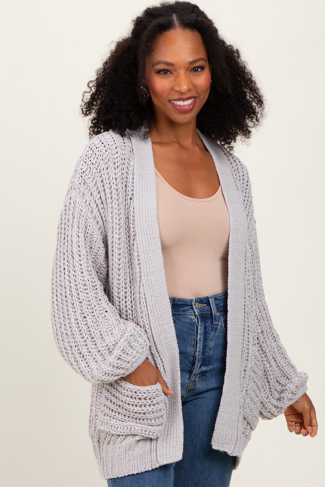 woman wearing a light gray open knit cardigan with side pockets and balloon sleeves paired with a nude top and blue jeans