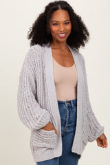 woman wearing a light gray open knit cardigan with side pockets and balloon sleeves paired with a nude top and blue jeans