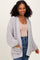 woman wearing a light gray open knit cardigan with side pockets and balloon sleeves paired with a nude top and blue jeans