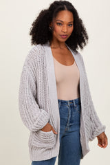 woman wearing a light gray chunky knit cardigan with oversized sleeves and front pockets, paired with a beige top and jeans