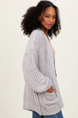 woman wearing a light gray chunky knit cardigan with pockets, paired with a beige top and blue jeans