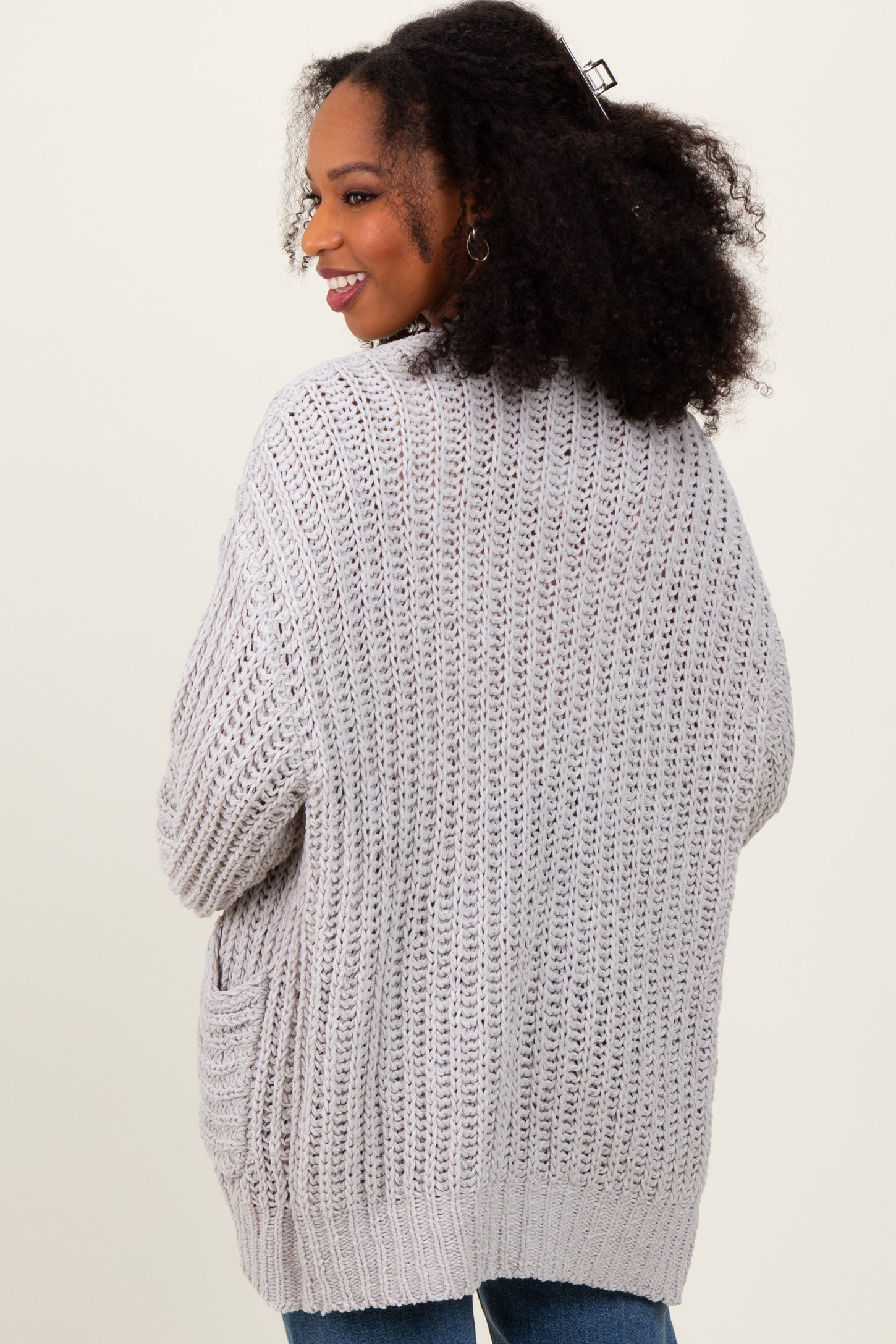 woman wearing a light gray open-knit oversized cardigan with pockets and curly hair styled down