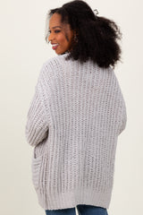 woman wearing a light gray open-knit oversized cardigan with pockets and curly hair styled down