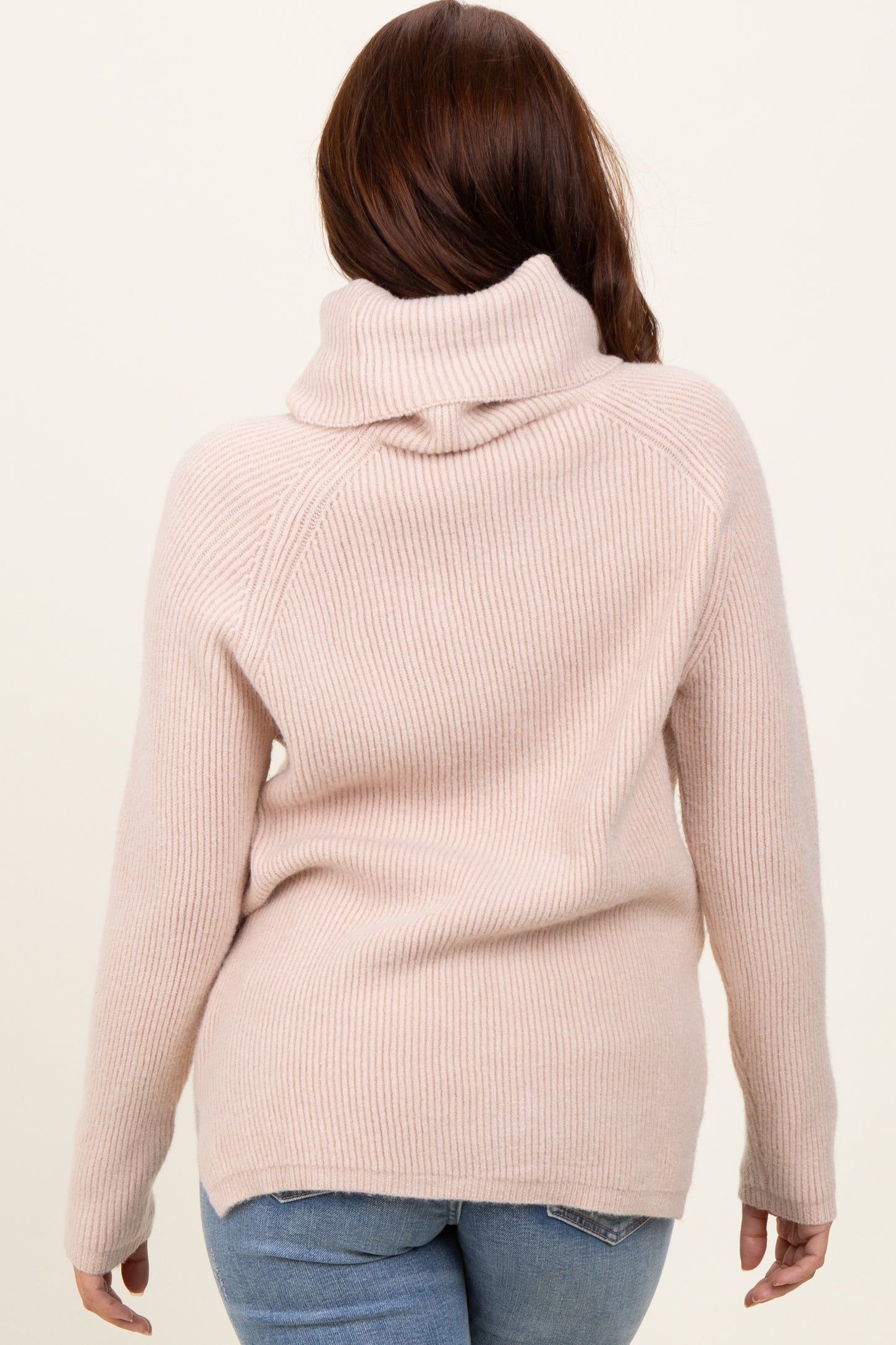 woman wearing a light pink ribbed sweater with a cowl neck and long sleeves, seen from the back