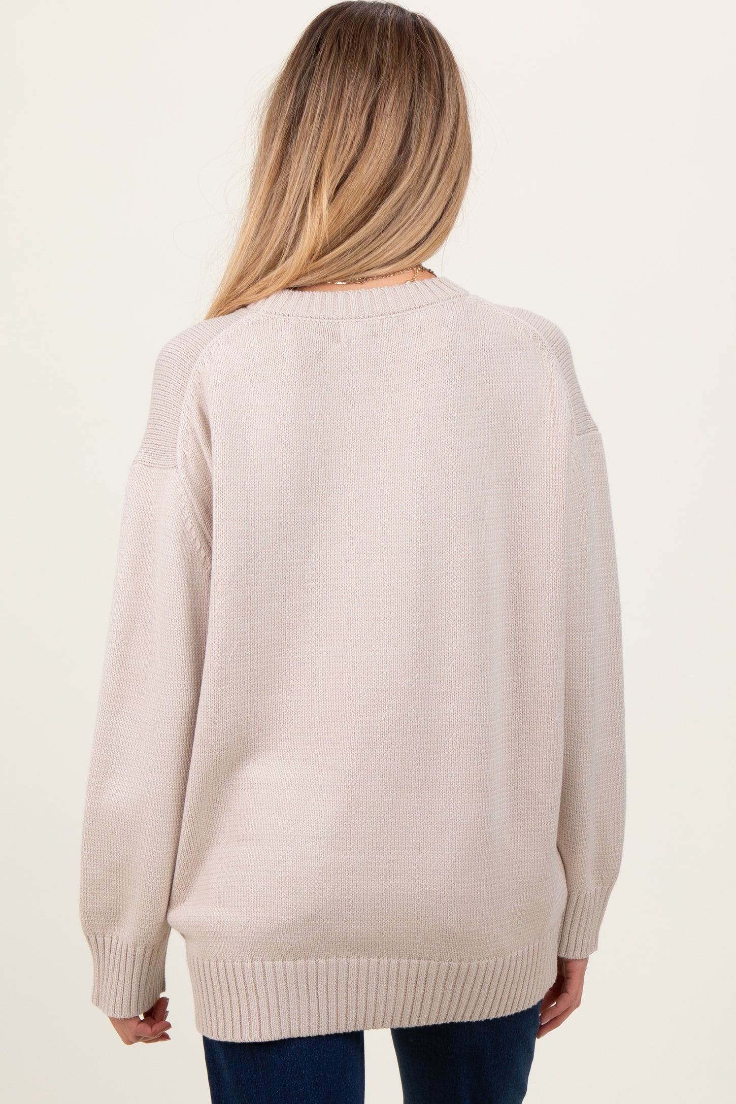 woman wearing a light beige oversized maternity sweater, shown from the back with a relaxed fit and ribbed details.