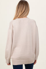 woman wearing a light beige oversized maternity sweater, shown from the back with a relaxed fit and ribbed details.