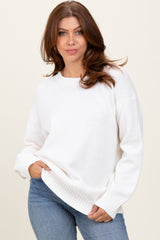 woman wearing a white oversized sweater with ribbed hem and long sleeves paired with blue jeans