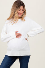 woman wearing a relaxed fit white maternity sweater and holding her baby bump, paired with denim jeans