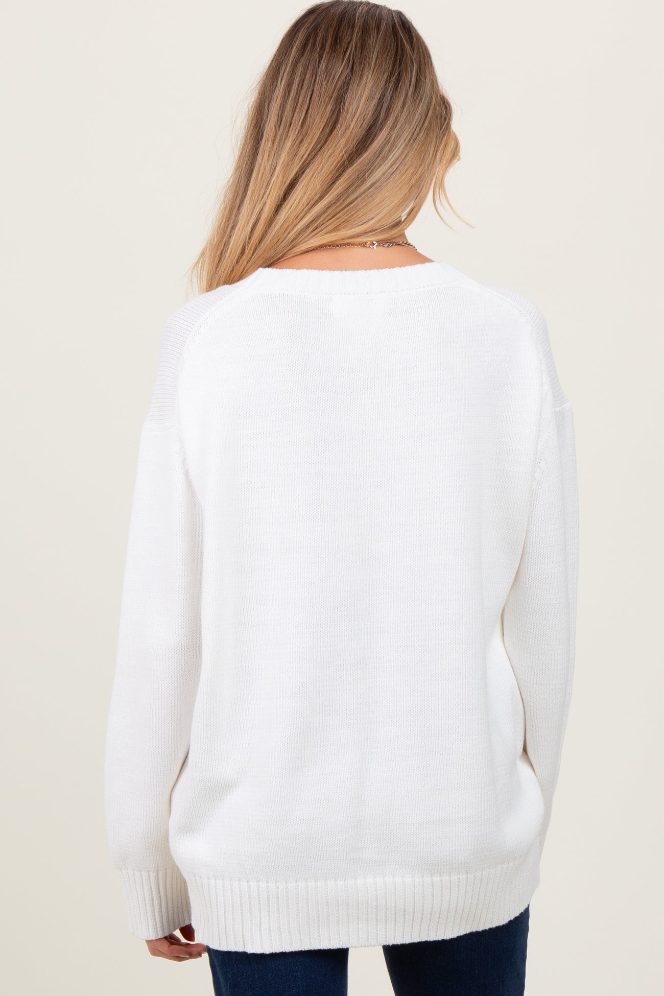 woman wearing a white oversized maternity sweater, seen from the back, paired with dark jeans