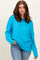 woman wearing a bright turquoise oversized sweater with a crew neckline and relaxed fit, paired with denim jeans