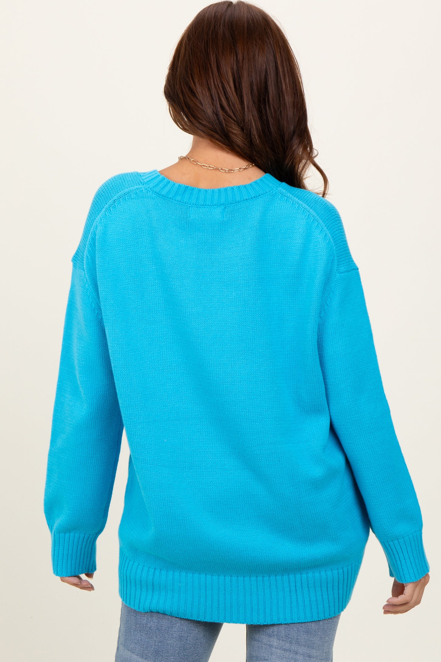 woman wearing a back view of a bright blue oversized sweater with ribbed cuffs and hem