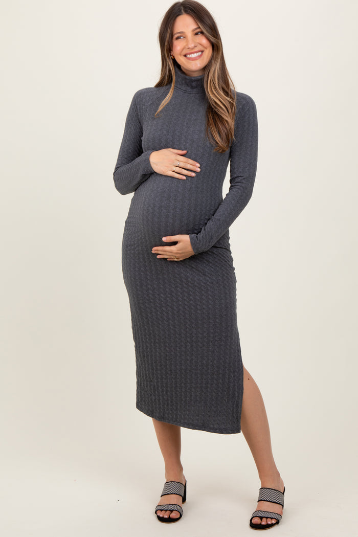 woman wearing a dark gray maternity dress with a turtleneck and side slit, holding her baby bump