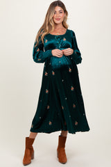 woman wearing a green floral velvet maternity dress with long sleeves and a baby bump