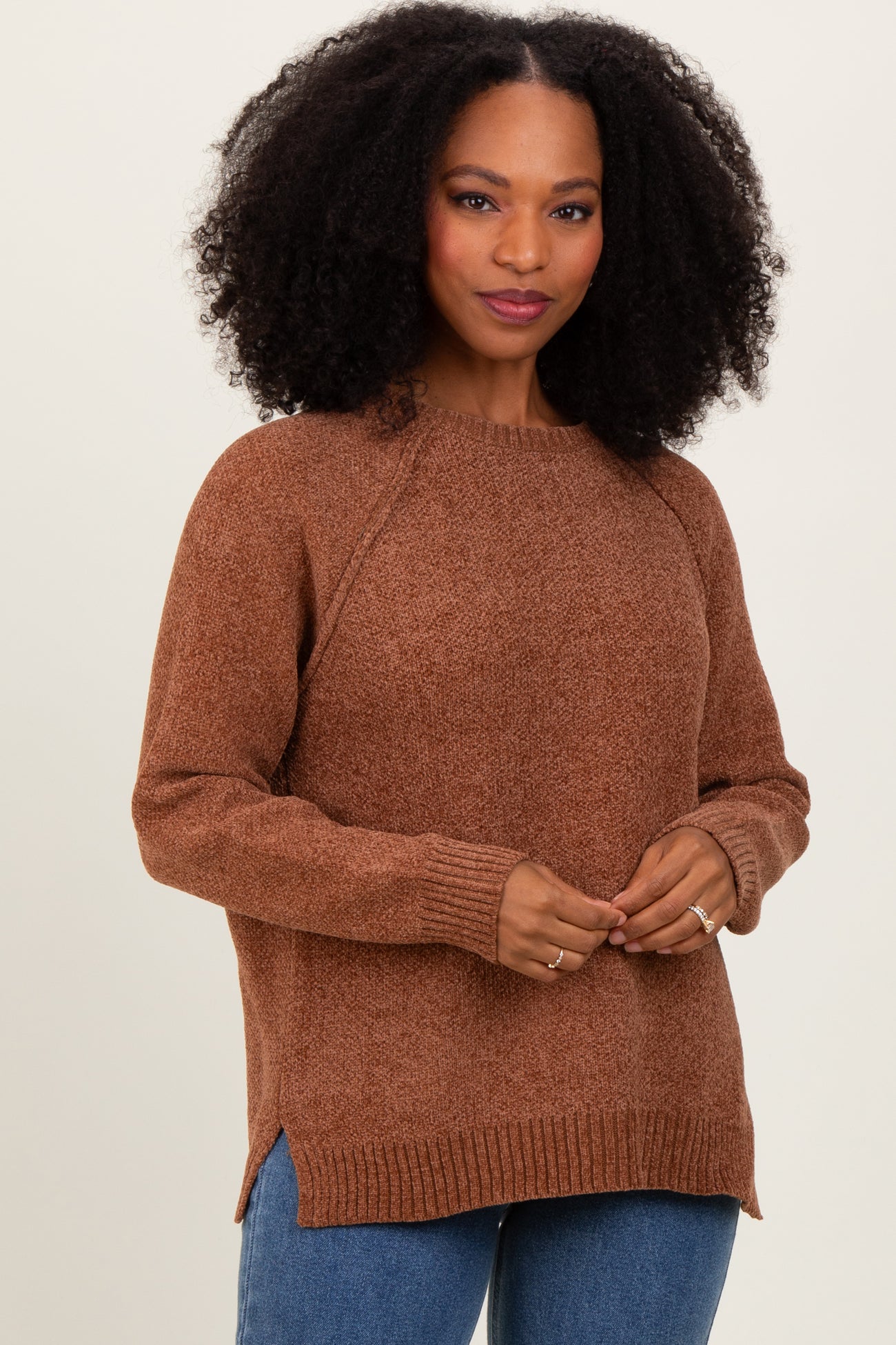 woman wearing a brown long sleeve sweater with raglan sleeves and side slits, styled with blue jeans