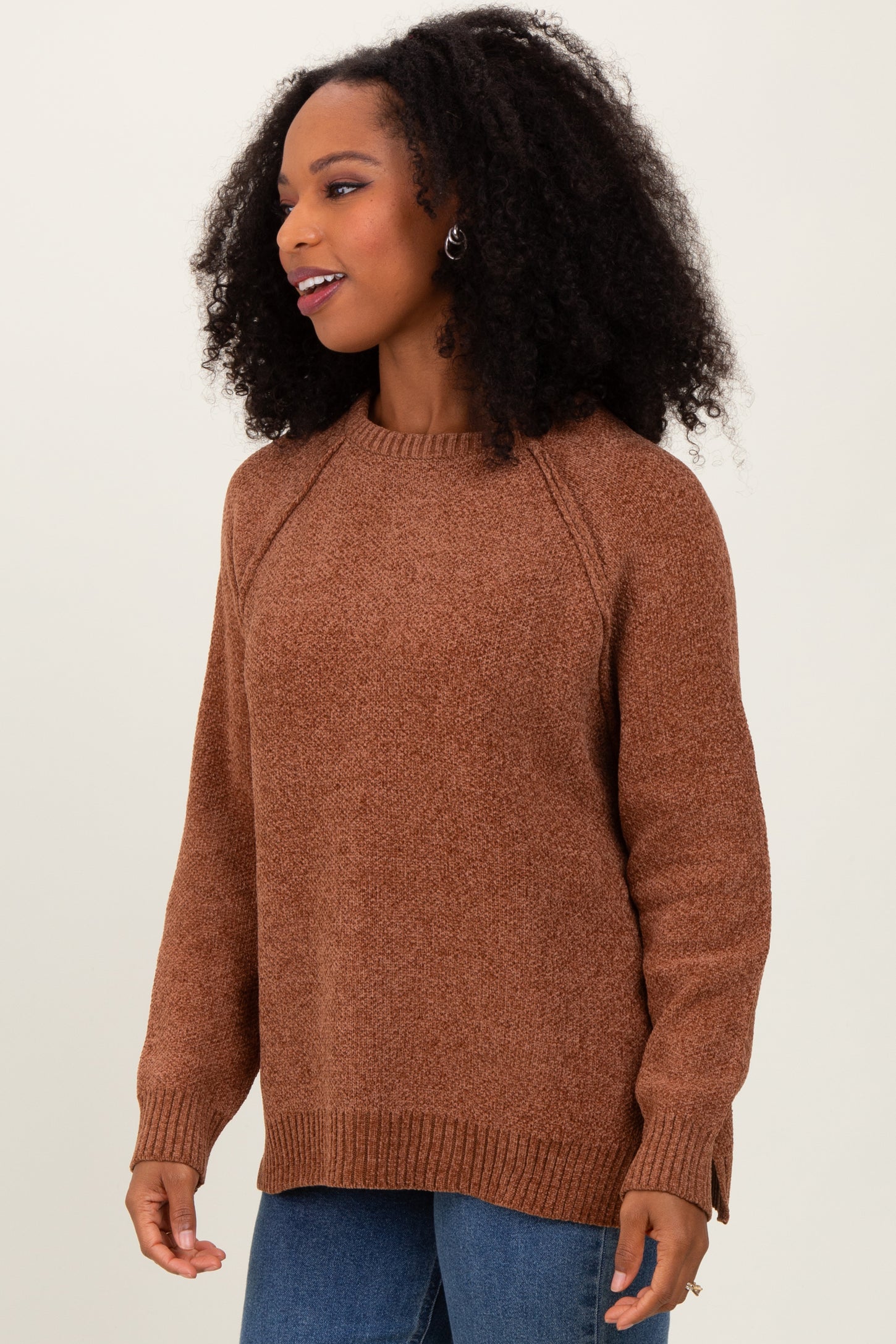 woman wearing a brown raglan sleeve sweater with a relaxed fit and side slits, styled with blue jeans