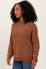 woman wearing a brown raglan sleeve sweater with a relaxed fit and side slits, styled with blue jeans