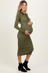 woman wearing a dark olive green ribbed maternity dress with long sleeves and a collar, cradling her baby bump