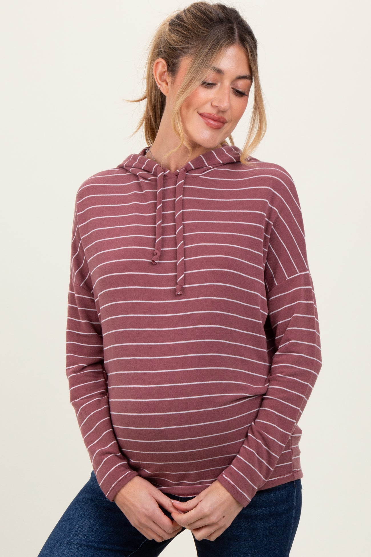woman wearing a striped maroon maternity hoodie and gently cradling her baby bump